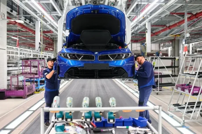 Dva radnika na proizvodnoj liniji u BMW fabrici montiraju prednji dio novog plavog BMW automobila