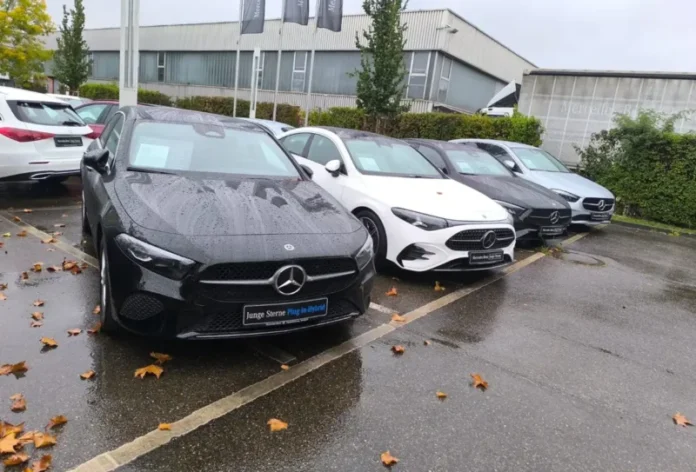 Četiri Mercedes-Benz A-Klasa vozila parkirana na placu auto salona, crni plug-in hybrid model u prvom planu, mokar asfalt i jesenje lišće nakon kiše